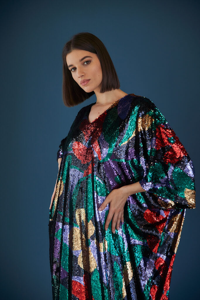 Model in shimmering dark Abaya against deep blue backdrop.